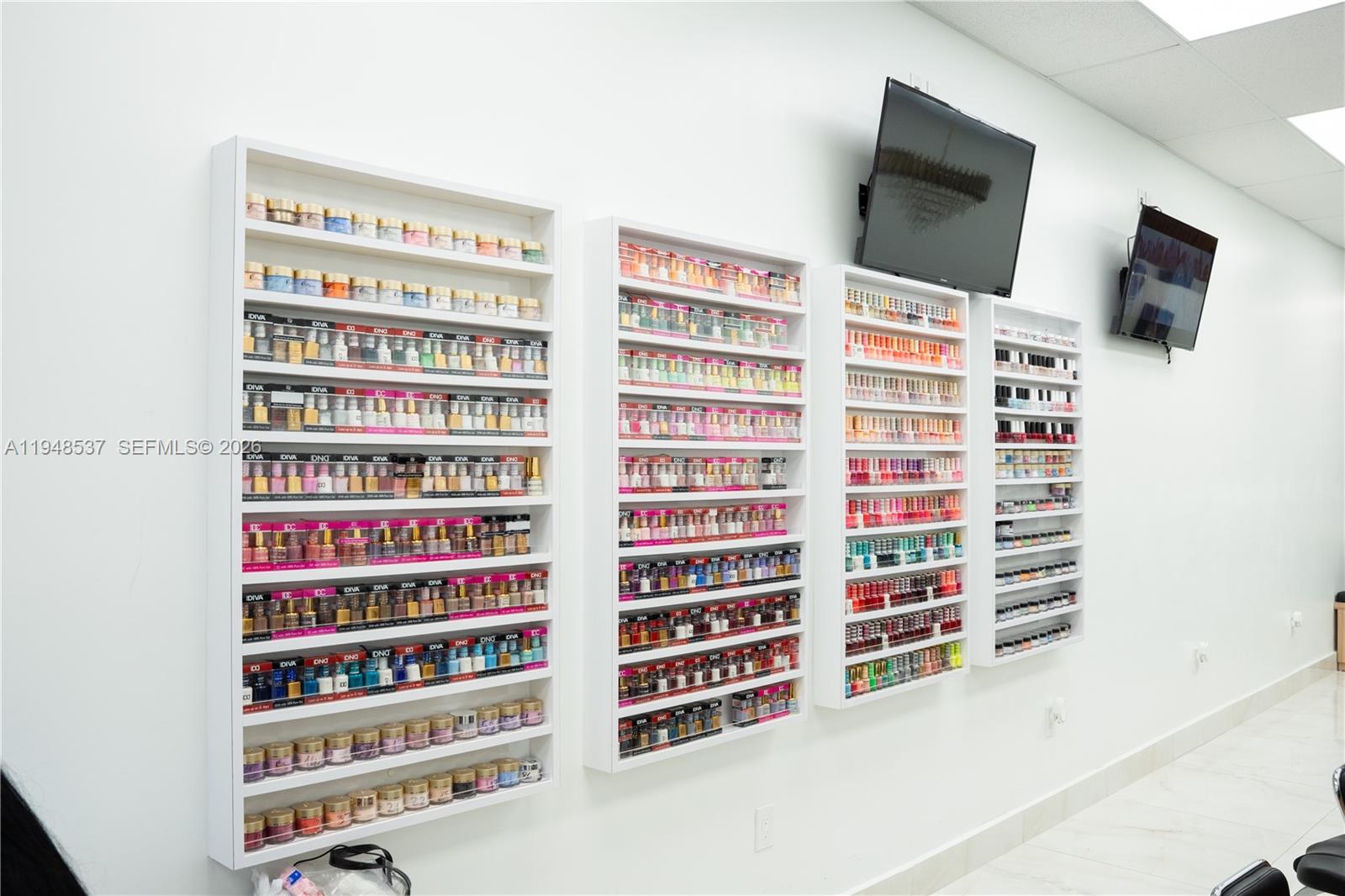 A nail salon wall features four white shelving units filled with various nail polish bottles — 2452 W 60st, Hialeah FL 33016, HIALEAH, FL
