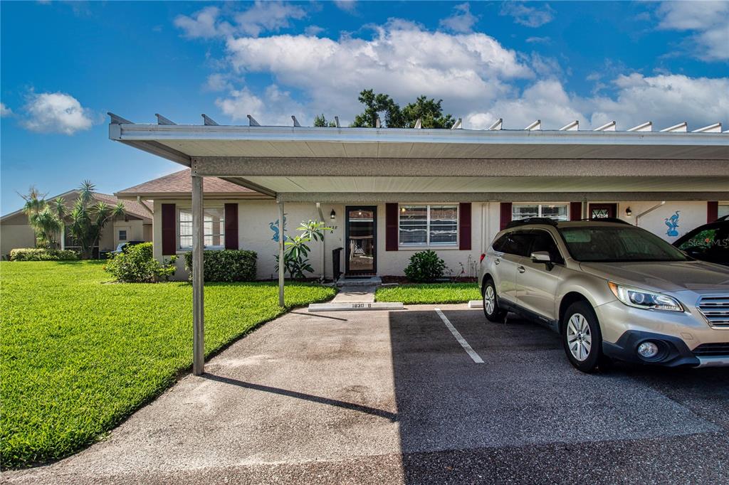 A single-story residential building features a covered carport and a parked SUV in front — 1828 FOXHUNT DRIVE UNIT A, SUN CITY CENTER, FL