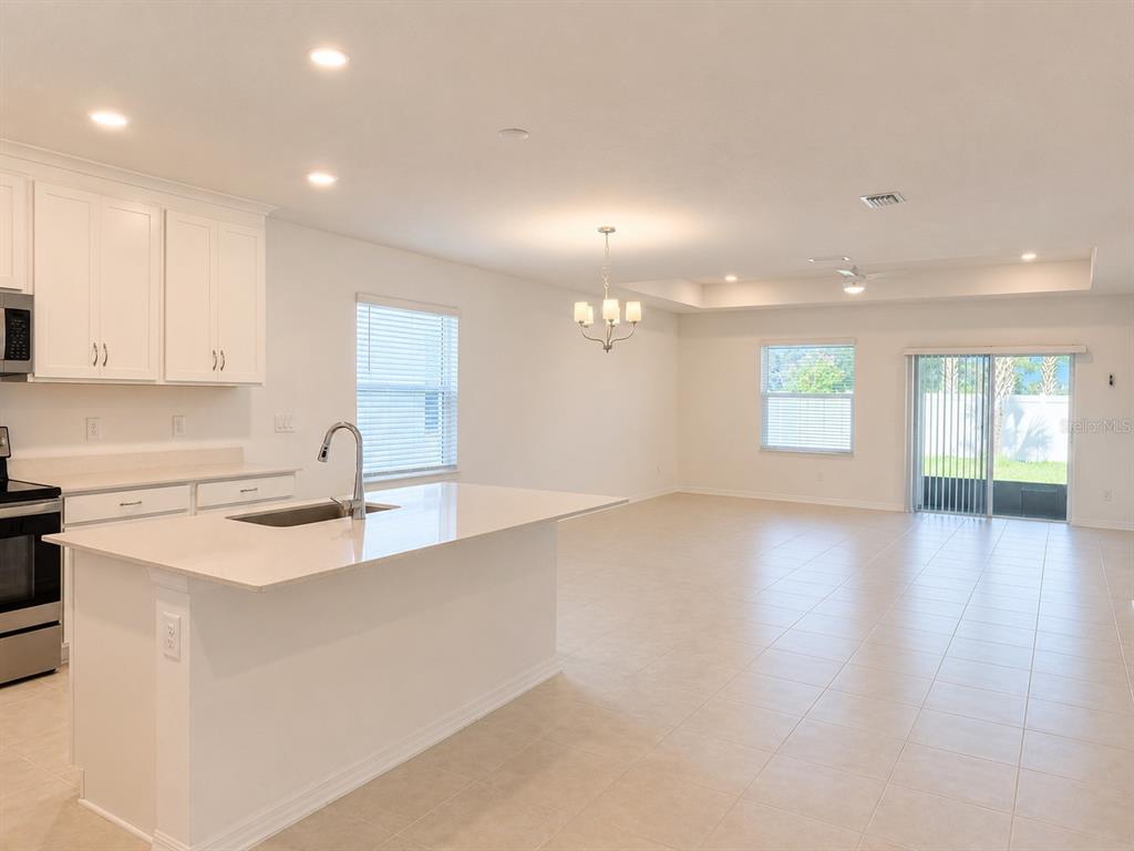 A kitchen with white cabinets and an island overlooks an open-concept living area with tile — 9706 LAST LIGHT GLEN, PARRISH, FL