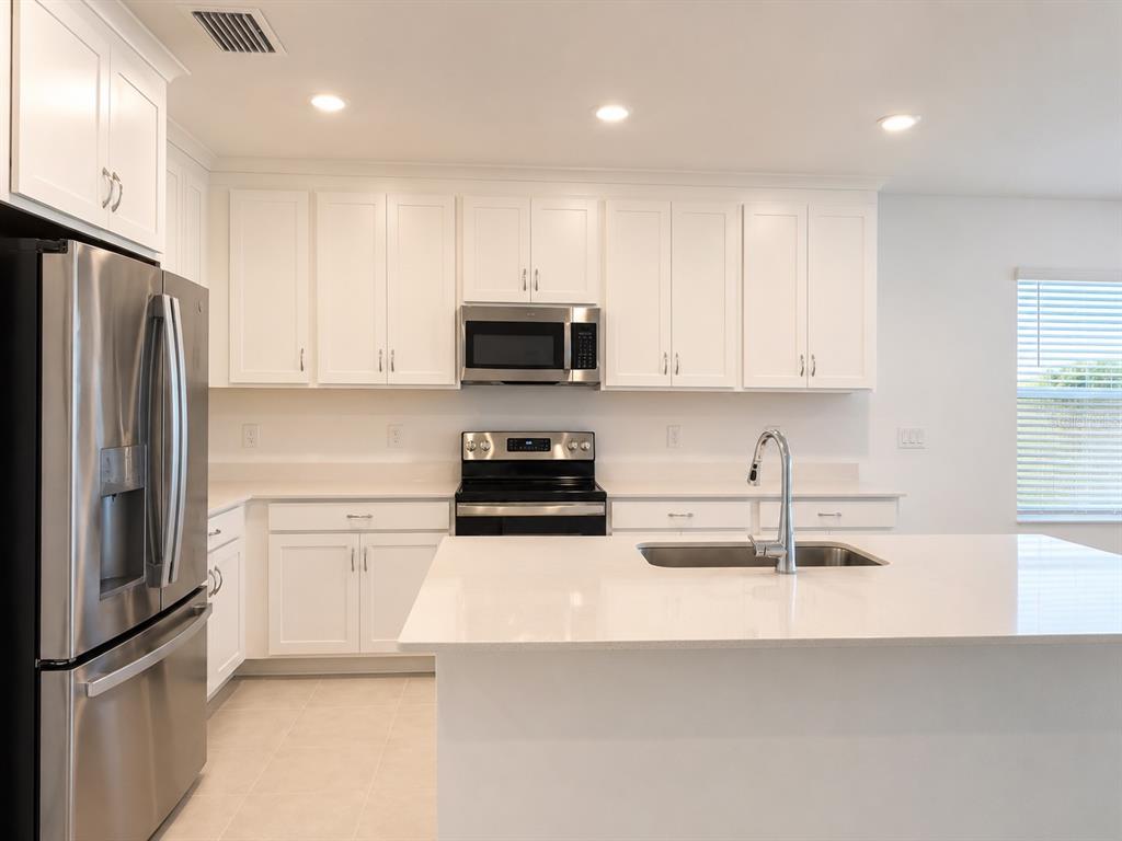 A modern kitchen features white cabinets, stainless steel appliances, and a large quartz-topped island — 9706 LAST LIGHT GLEN, PARRISH, FL
