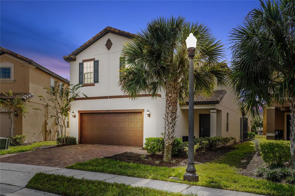 A two-story suburban house with a garage, palm trees, and a street lamp at dusk — 5505 MISTY OAK CIRCLE, DAVENPORT, FL