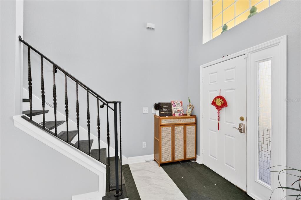 An entryway features a staircase with black railings, a white front door, and tiled flooring — 13538 HIDDEN FOREST CIRCLE, ORLANDO, FL