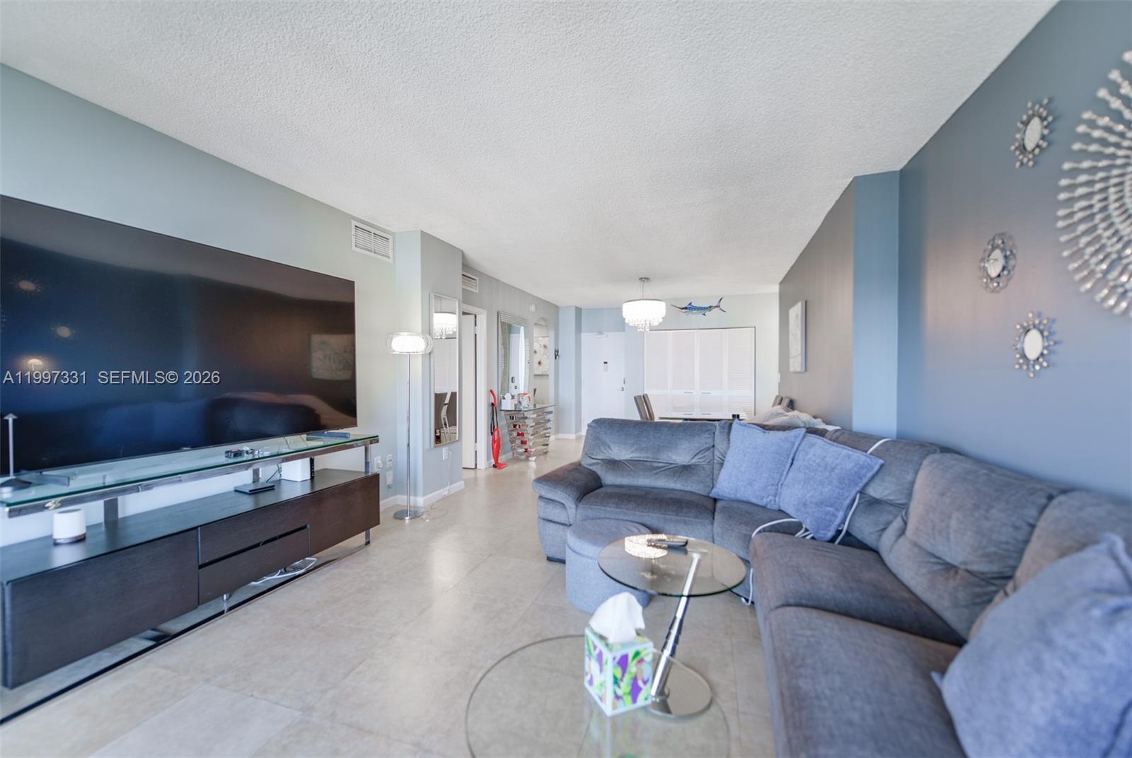 A living room features a large television, a grey sectional sofa, and light tile flooring — 1950 S Ocean Dr # 20D, Hallandale Beach FL 33009, HALLANDALE BEACH, FL