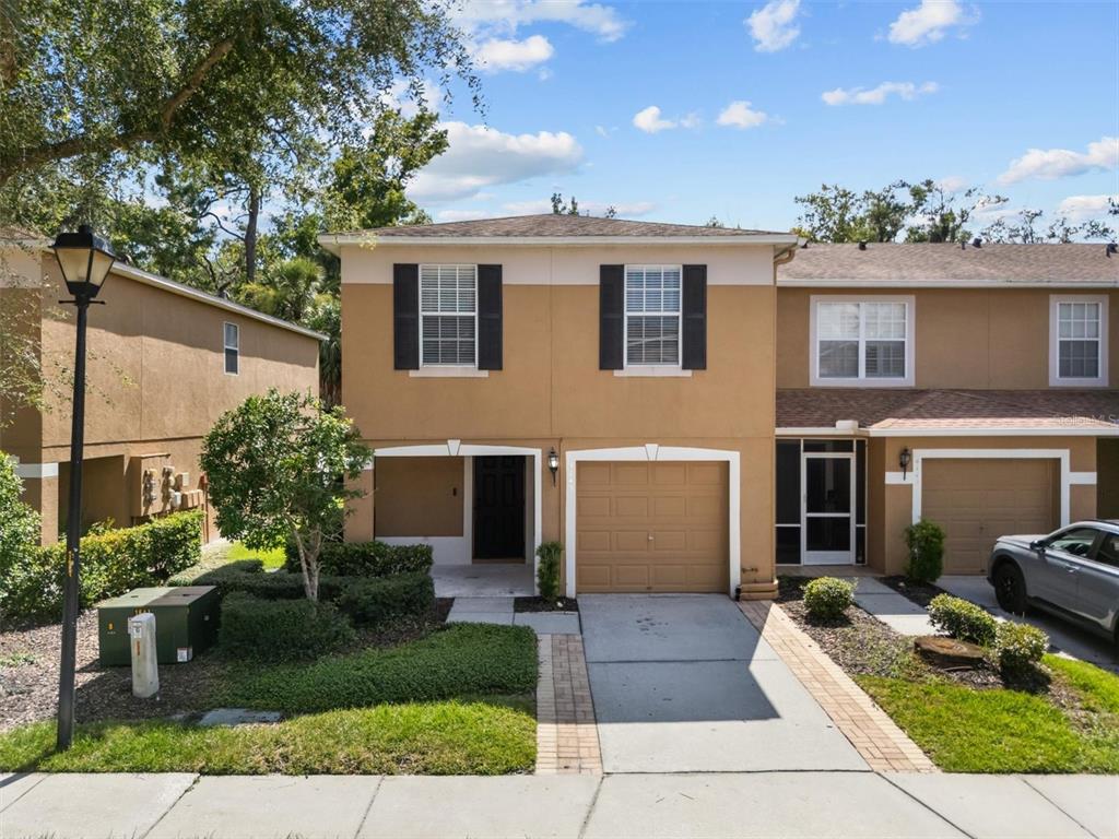 A two-story tan townhouse with a single-car garage and a small front lawn — 4143 WINDING RIVER WAY, LAND O LAKES, FL