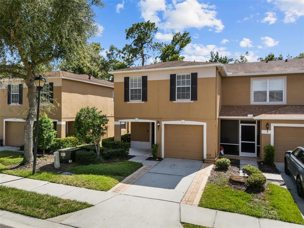 A two-story tan townhouse with a single-car garage, a screened entryway, and a paved driveway — 4143 WINDING RIVER WAY, LAND O LAKES, FL