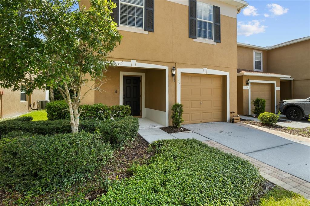 A two-story tan stucco townhouse with a front-facing garage and a landscaped yard — 4143 WINDING RIVER WAY, LAND O LAKES, FL
