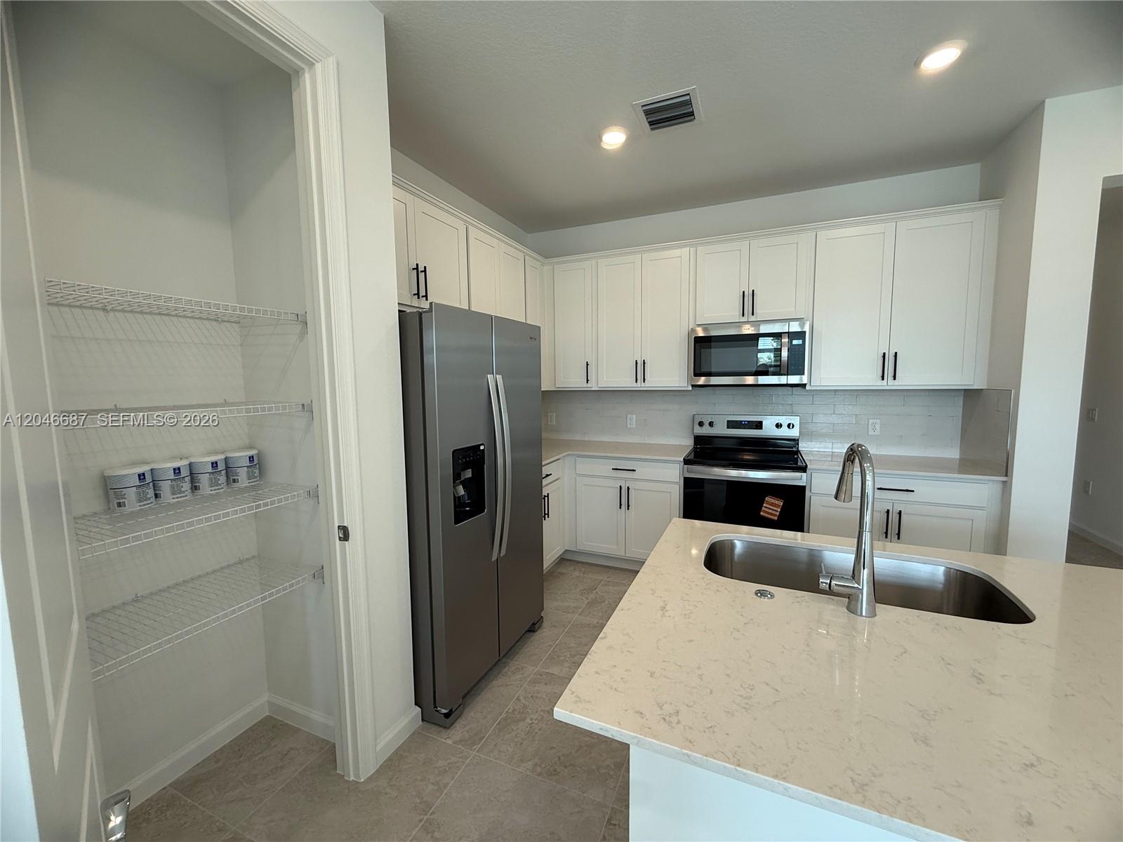 A kitchen features white cabinets, stainless steel appliances, a quartz island, and an open pantry — 4286 Efendi Drive, Lantana FL 33462, LANTANA, FL