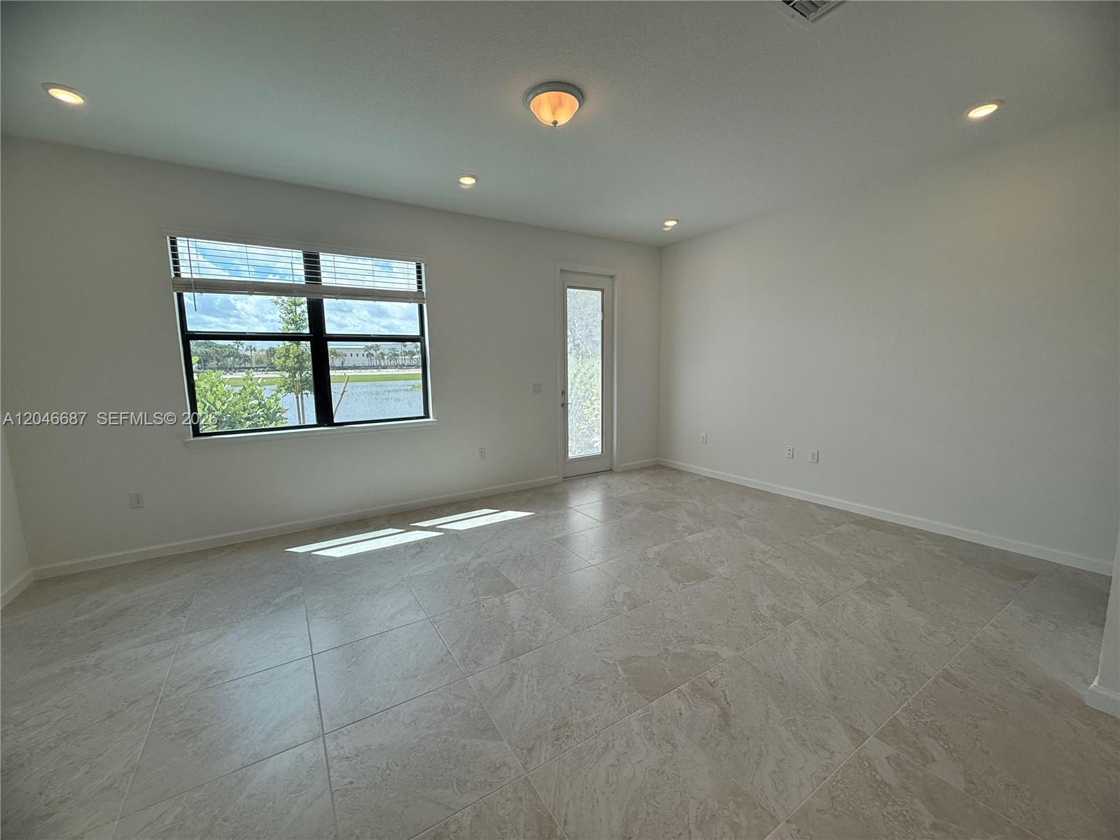 A bright, empty room features large light-colored floor tiles, recessed lighting, and a glass door — 4286 Efendi Drive, Lantana FL 33462, LANTANA, FL