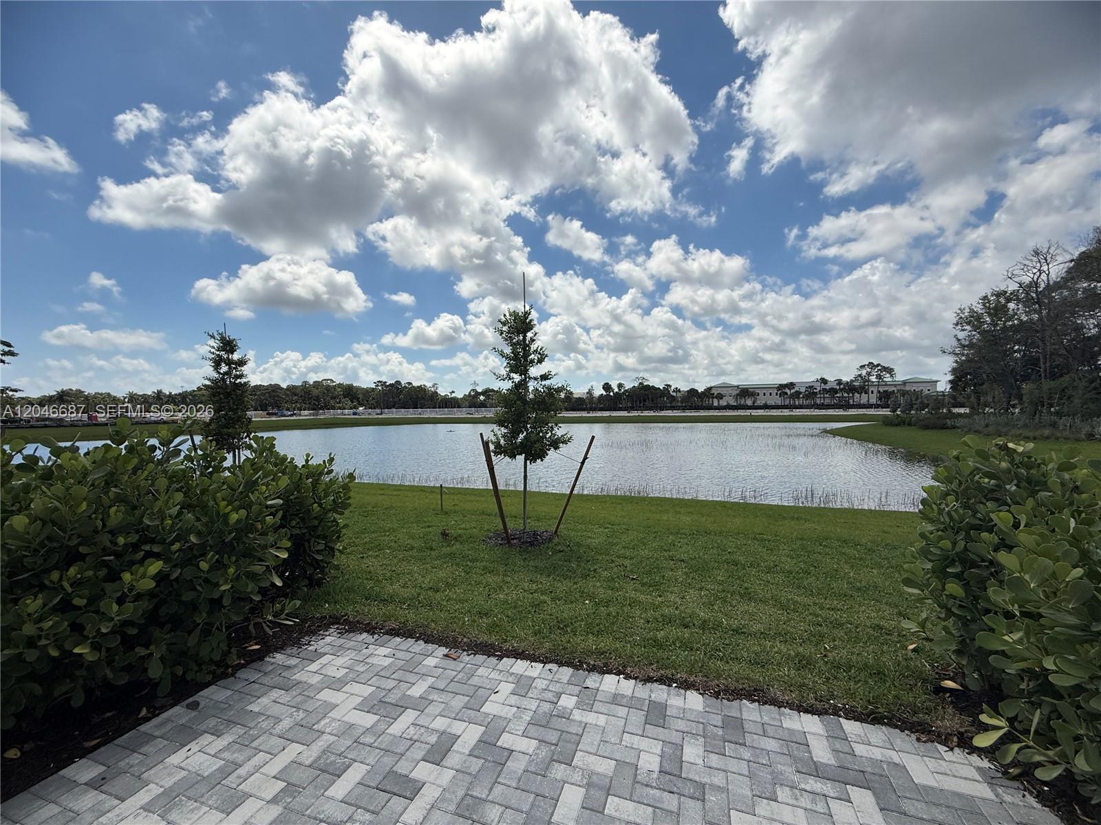 A paved patio overlooks a grassy lawn, a small tree, and a large pond — 4286 Efendi Drive, Lantana FL 33462, LANTANA, FL