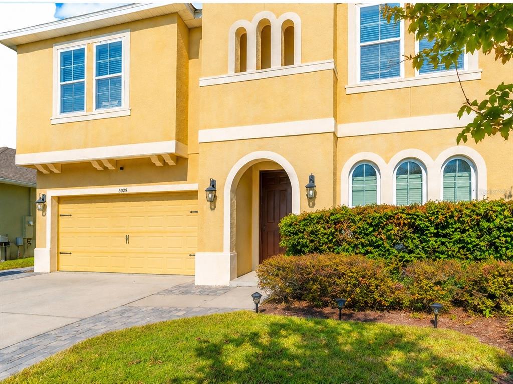 A two-story yellow stucco house features a two-car garage, arched windows, and a front entrance — 1889 RUSTIC FALLS DRIVE, KISSIMMEE, FL