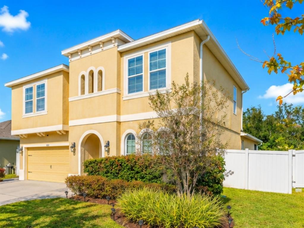 A two-story yellow stucco house with a two-car garage and a white vinyl fence — 1889 RUSTIC FALLS DRIVE, KISSIMMEE, FL