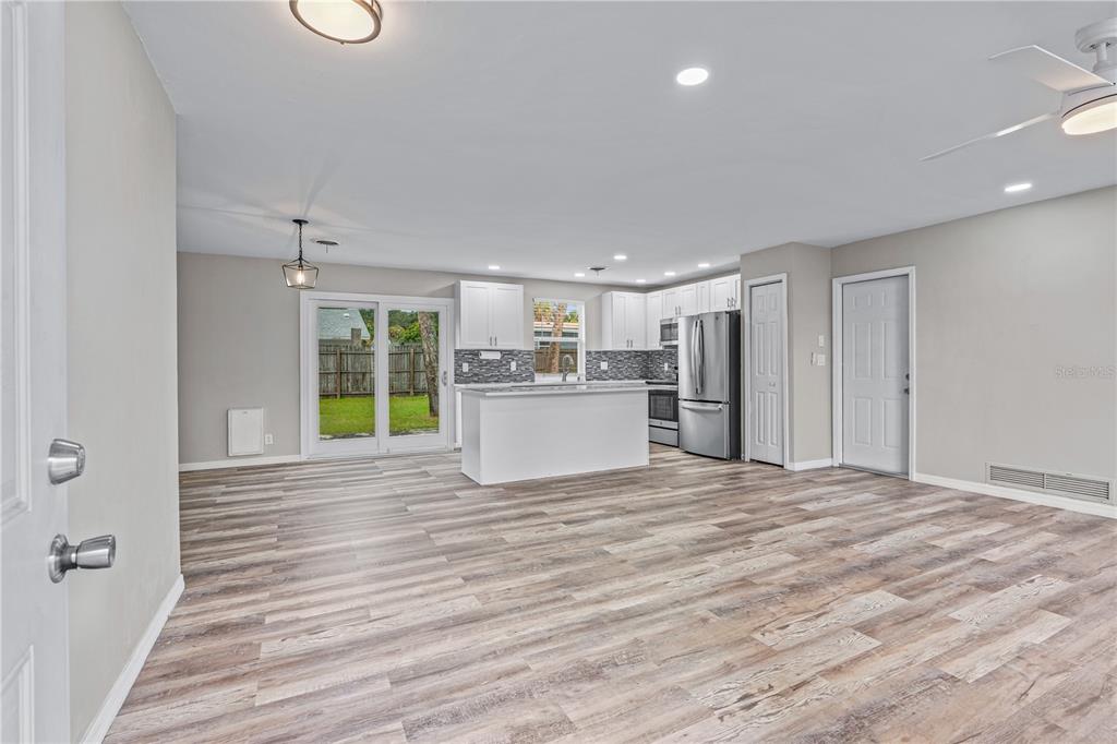An open-concept kitchen and living area features white cabinetry, a center island, and wood-look flooring — 882 W COQUINA DRIVE, DAYTONA BEACH, FL
