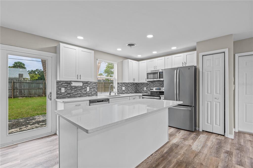 A modern kitchen features white cabinets, a quartz island, stainless steel appliances, and wood-look flooring — 882 W COQUINA DRIVE, DAYTONA BEACH, FL