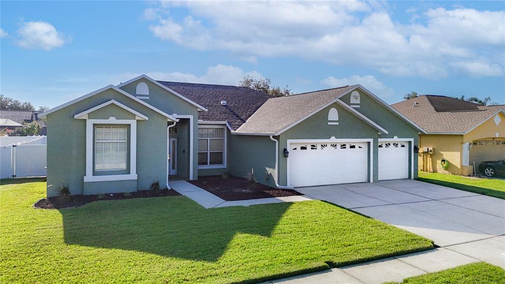 A single-story house with a green stucco exterior, a three-car garage, and a front lawn — 24807 BLAZING TRAIL WAY, LAND O LAKES, FL