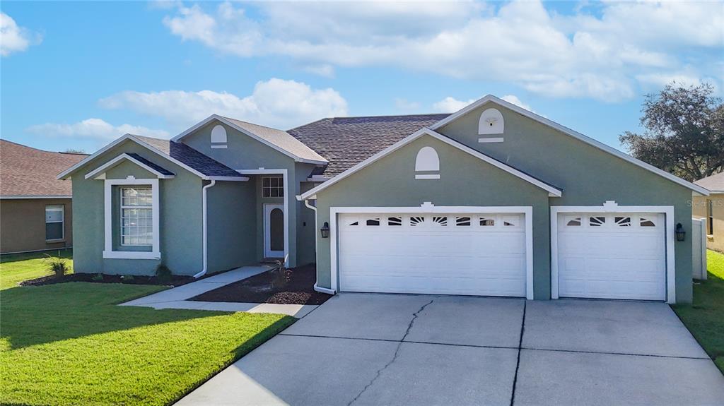 A single-story house with a green stucco exterior, a three-car garage, and a front lawn — 24807 BLAZING TRAIL WAY, LAND O LAKES, FL
