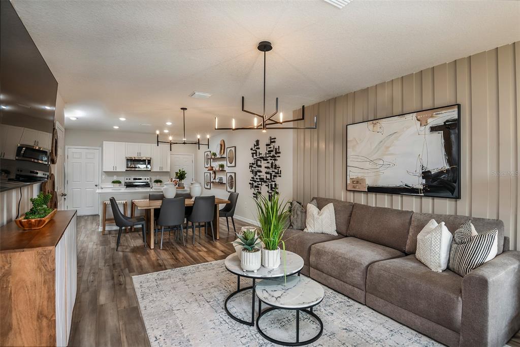An open-concept living and dining area features wood-look flooring, a gray sofa, and modern lighting — 9880 PELICAN COAST DRIVE, DADE CITY, FL