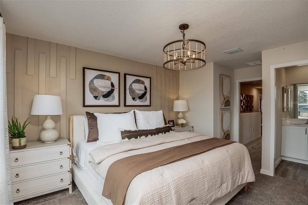 A bedroom features a bed with brown bedding, a chandelier, and a paneled accent wall — 9880 PELICAN COAST DRIVE, DADE CITY, FL