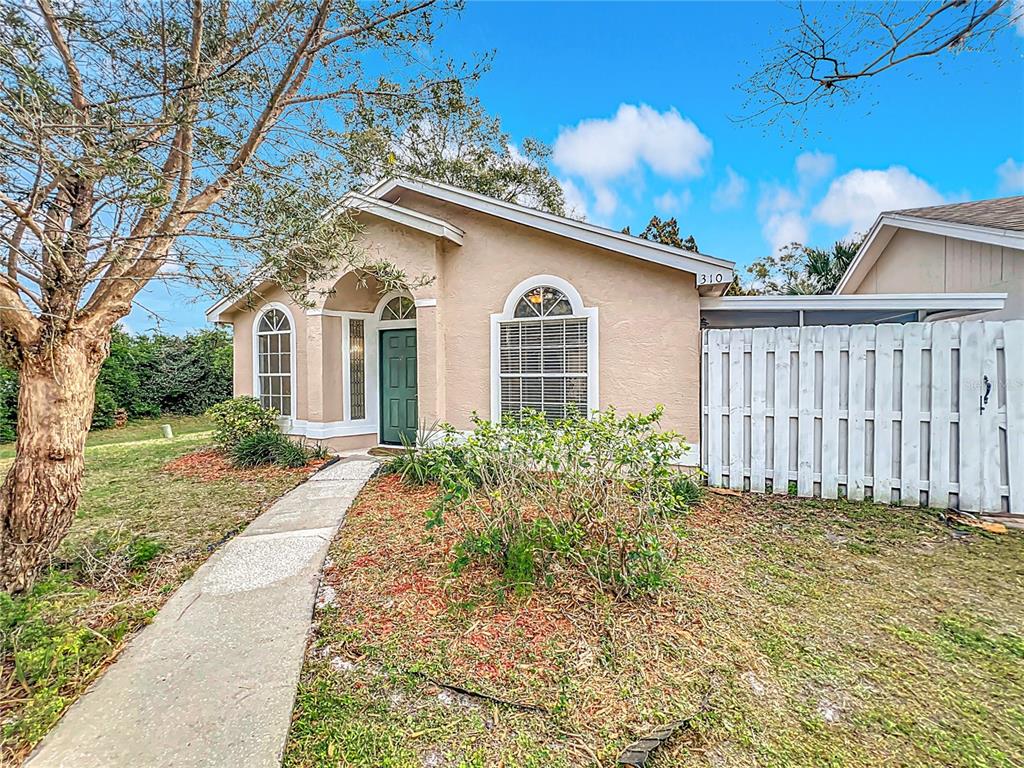 A single-story house with tan stucco siding, a green front door, and a white fence — 310 SUNVISTA COURT, SANFORD, FL