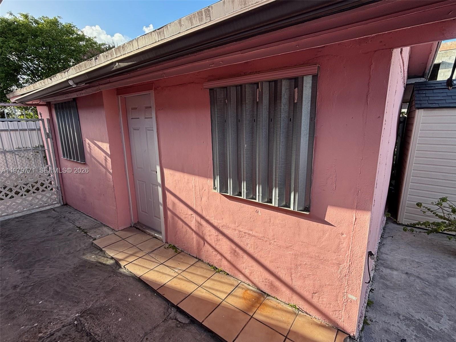 The exterior of a pink stucco building features a white door and metal storm shutters — 3533 NW 2nd Ter, Miami FL 33125, MIAMI, FL
