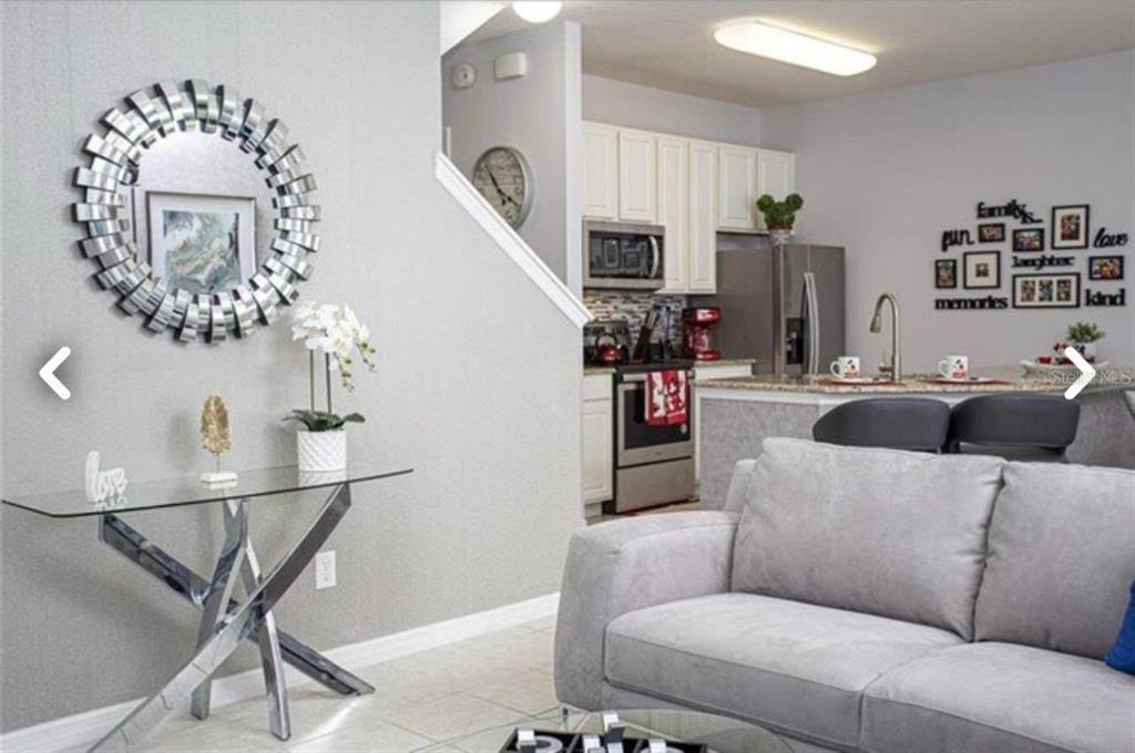 A living room with a glass console table and mirror leads to an open kitchen area — 1050 LAS FUENTES DRIVE, KISSIMMEE, FL