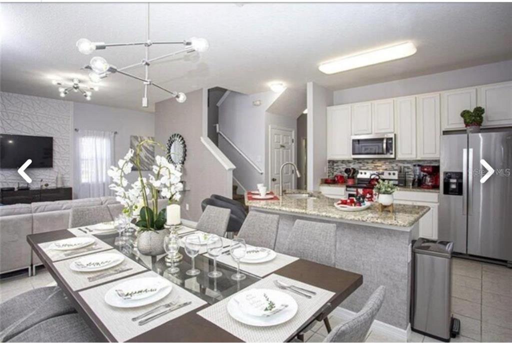 An open-concept dining area and kitchen featuring a glass-top table, granite countertops, and stainless appliances — 1050 LAS FUENTES DRIVE, KISSIMMEE, FL
