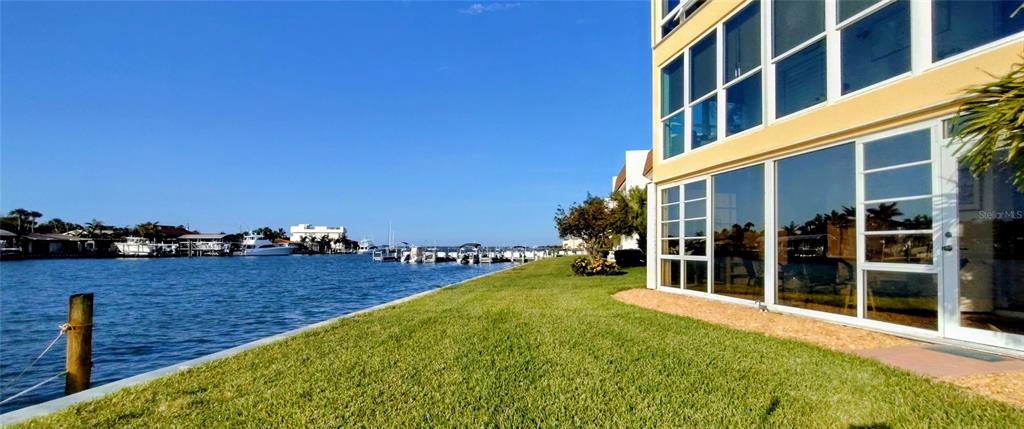 A grassy lawn borders a canal with docked boats next to a multi-story building — 1351 BAYSHORE DRIVE UNIT 108, FORT PIERCE, FL