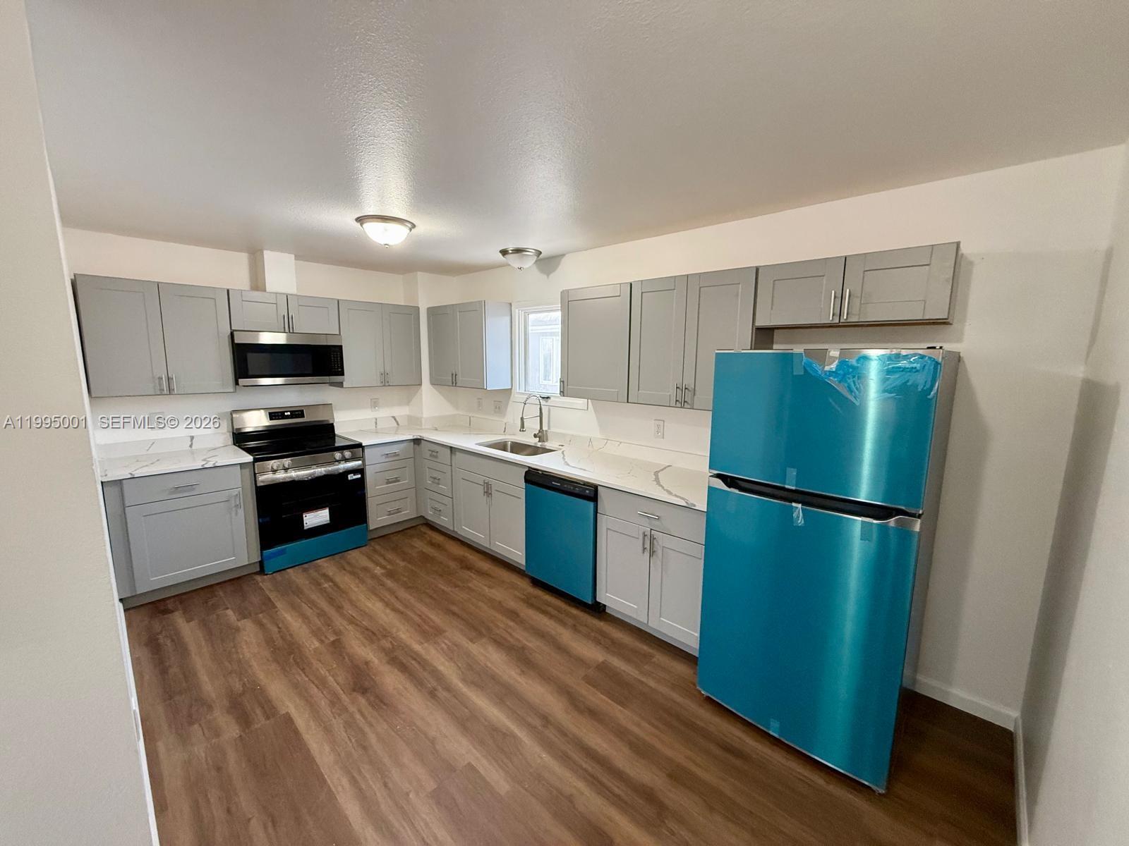 A kitchen features grey cabinets, white countertops, wood-look flooring, and new appliances with protective film — 423 N Lane ST # 4, AK 99508, AK