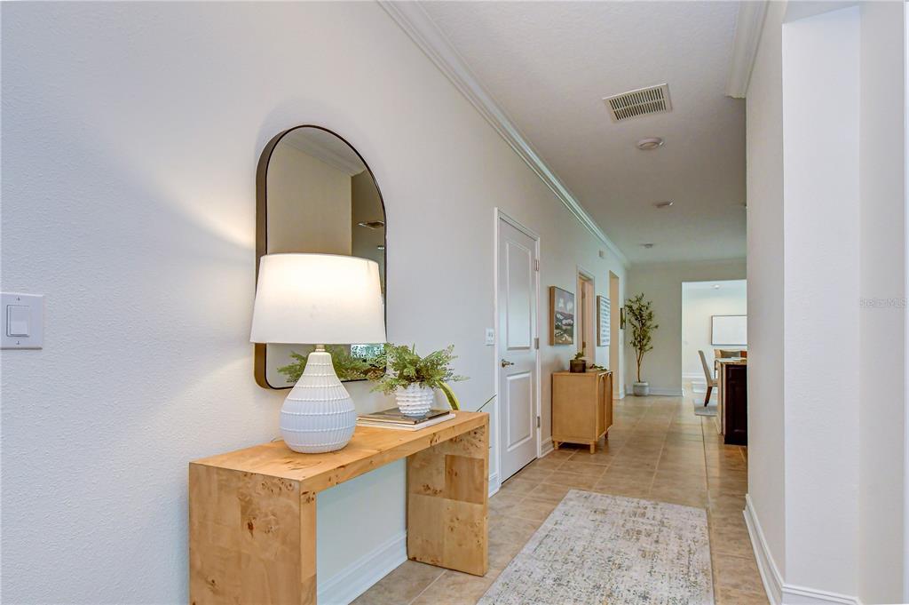 A hallway features a light wood console table, a lamp, a mirror, and tiled flooring — 4749 ROLLING GREEN DRIVE, WESLEY CHAPEL, FL