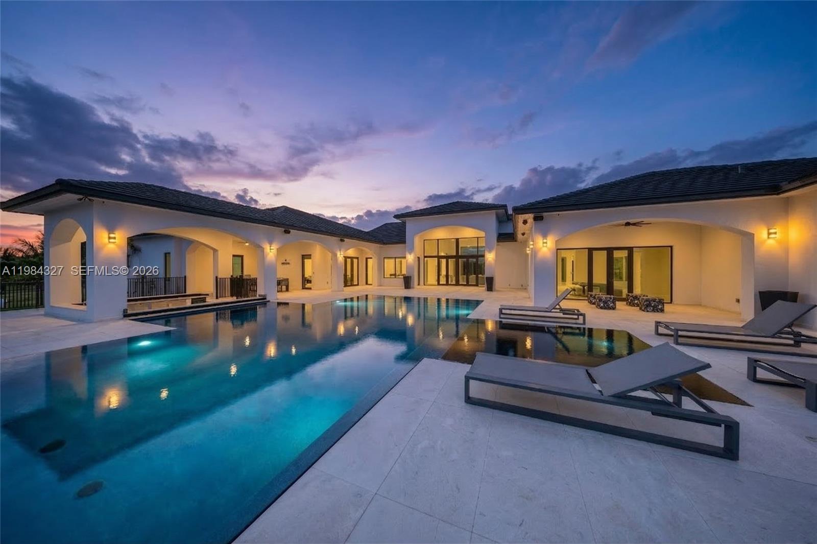 A modern house with a large swimming pool and patio area at dusk — 15620 SW 188th Ct, Miami FL 33187, MIAMI, FL