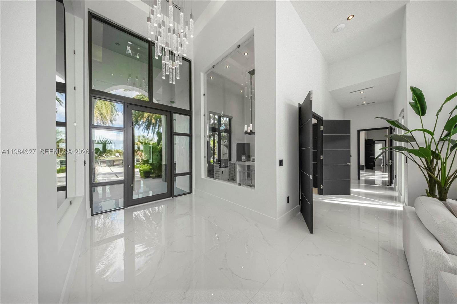 A bright, modern entryway features white marble floors, a tall glass door, and a chandelier — 15620 SW 188th Ct, Miami FL 33187, MIAMI, FL