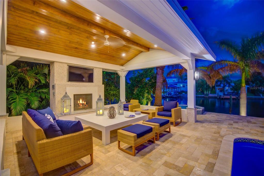 A covered outdoor patio features a fireplace, television, wicker furniture, and a view of a canal — 807 SNUG ISLAND, CLEARWATER, FL