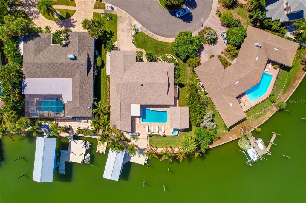 An aerial view shows three waterfront houses with swimming pools and private boat docks — 807 SNUG ISLAND, CLEARWATER, FL