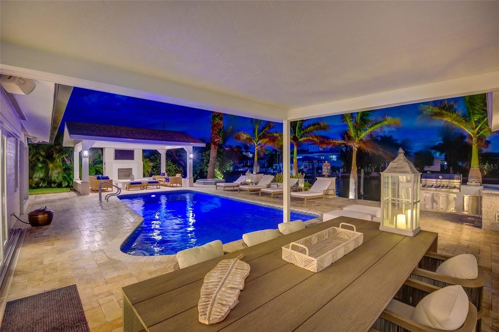 A covered patio overlooks a swimming pool and a canal at night — 807 SNUG ISLAND, CLEARWATER, FL