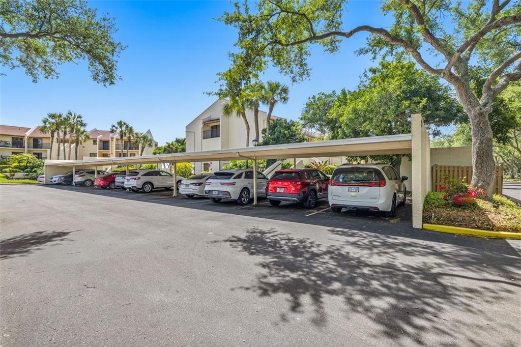 A row of parked cars sits under a covered carport in a residential parking lot — 7520 SUNSHINE SKYWAY LANE S UNIT T22, ST PETERSBURG, FL