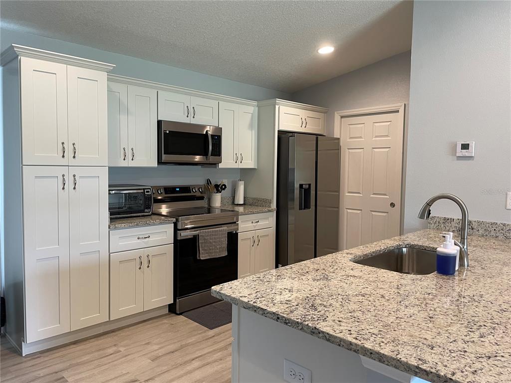 A kitchen features white cabinetry, granite countertops, stainless steel appliances, and a central island — 16060 SW 23RD COURT ROAD, OCALA, FL