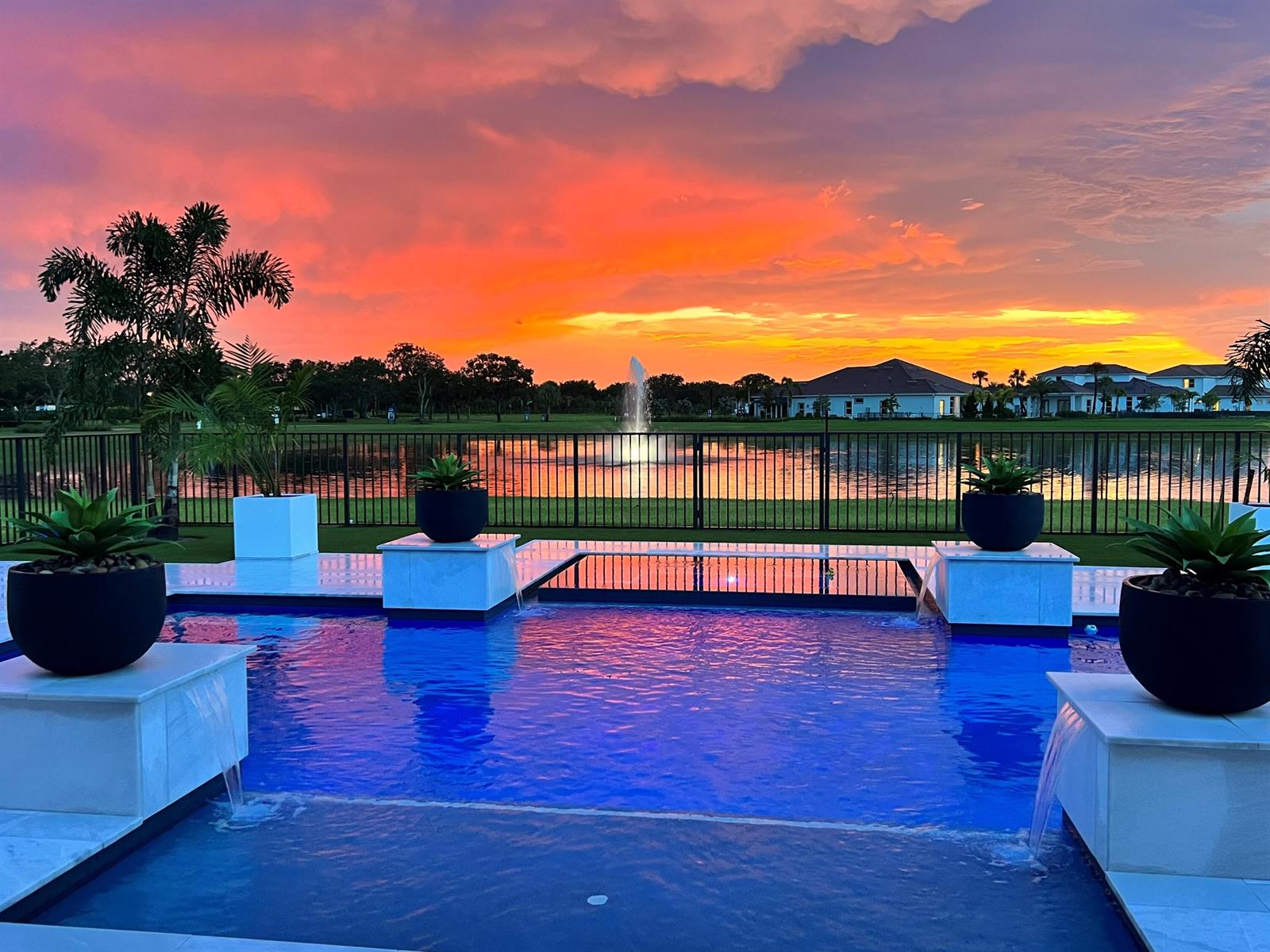 A swimming pool with water features overlooks a lake and a sunset sky — 20124 SE Bridgewater Drive, Jupiter FL 33458, JUPITER, FL