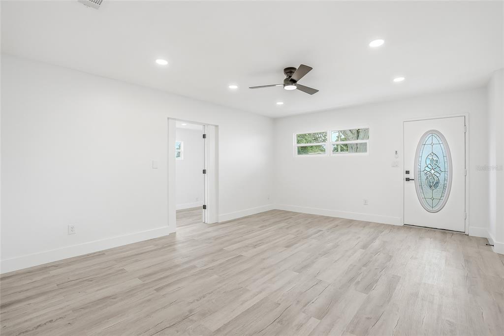 A bright, empty living room features white walls, light wood-look flooring, a ceiling fan, and a front door — 529 FIREFLY LANE, APOLLO BEACH, FL
