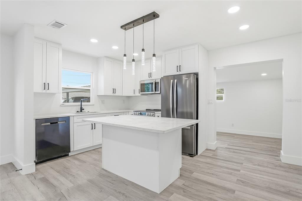 A modern kitchen features white cabinetry, stainless steel appliances, a marble-topped island, and light flooring — 529 FIREFLY LANE, APOLLO BEACH, FL