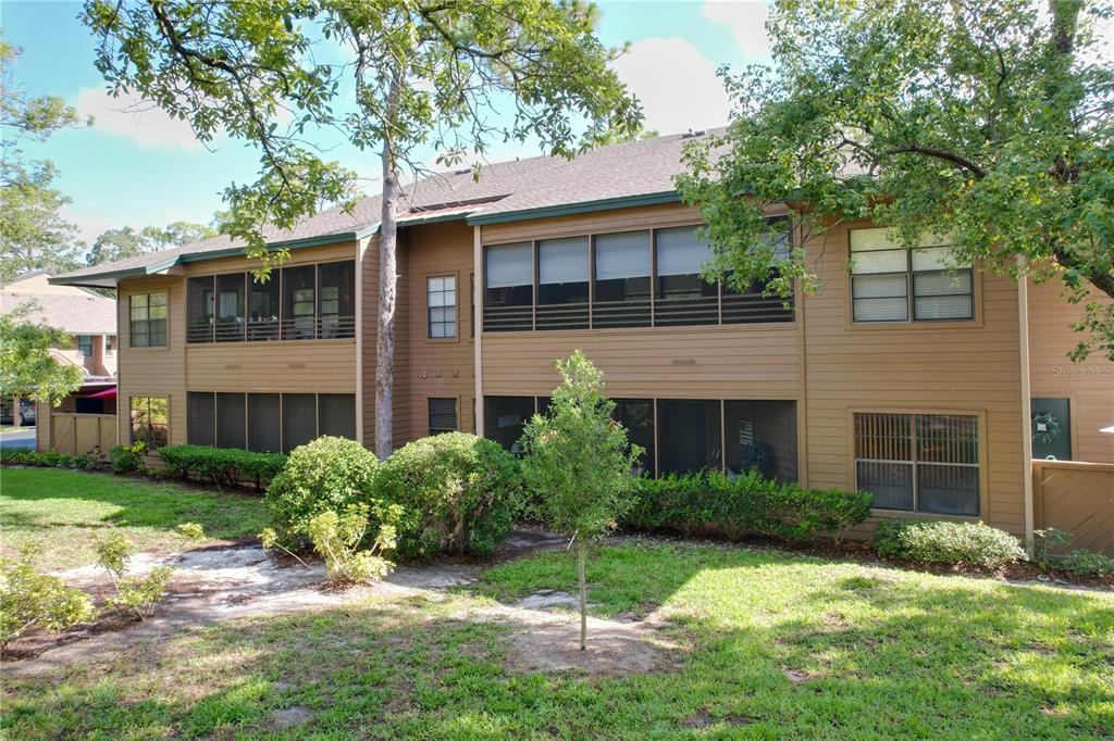 A two-story brown apartment building features screened-in porches and surrounding landscaping — 1006 LENNOX ROAD W UNIT 1006, PALM HARBOR, FL