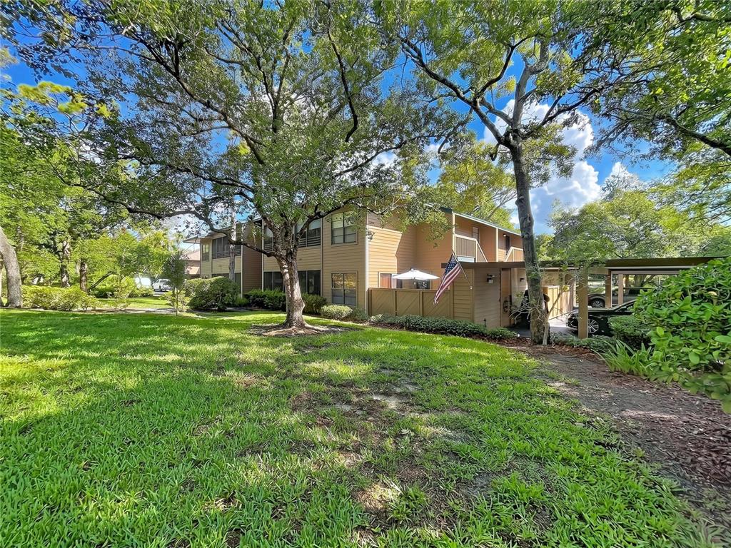 A two-story tan apartment building with a covered carport and a grassy lawn — 1006 LENNOX ROAD W UNIT 1006, PALM HARBOR, FL