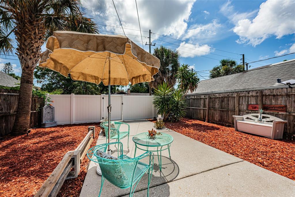 A backyard patio features a concrete slab, teal metal furniture, and a tan umbrella — 547 15TH STREET N, ST PETERSBURG, FL