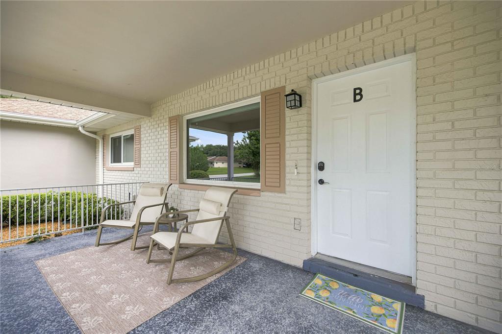 A covered porch features a white brick exterior, two rocking chairs, and a front door — 8891 SW 96TH LANE UNIT B, OCALA, FL