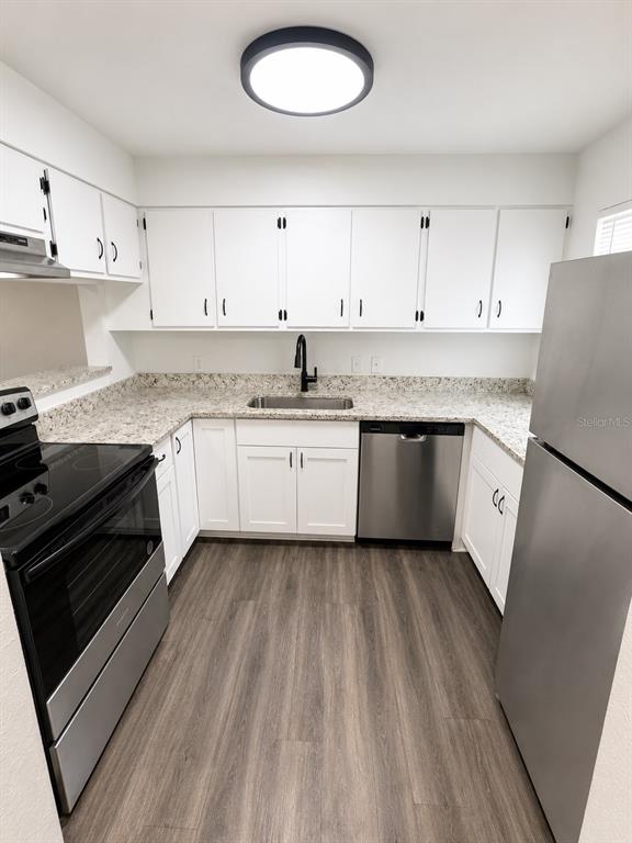A kitchen features white cabinets, stainless steel appliances, speckled countertops, and wood-look flooring — 1717-1717 NE 2ND STREET, OCALA, FL