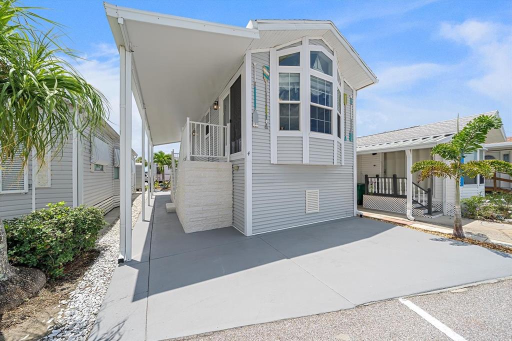A light gray mobile home with a covered carport, bay window, and exterior paddle decorations — 4 BASIN STREET, PALMETTO, FL
