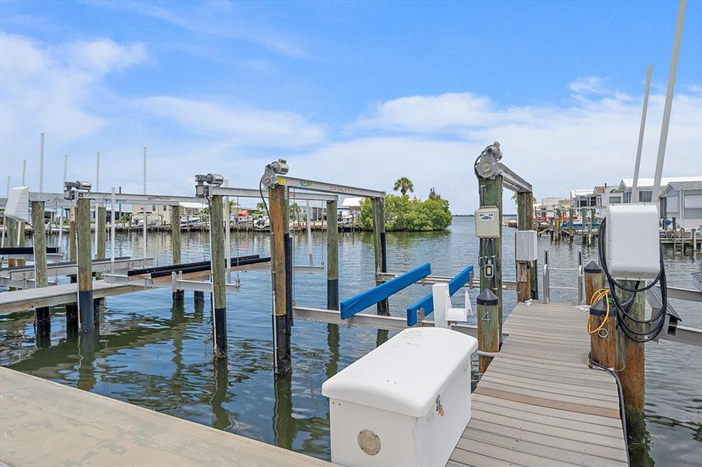 A wooden dock features a boat lift with blue bunks and a white storage box — 4 BASIN STREET, PALMETTO, FL