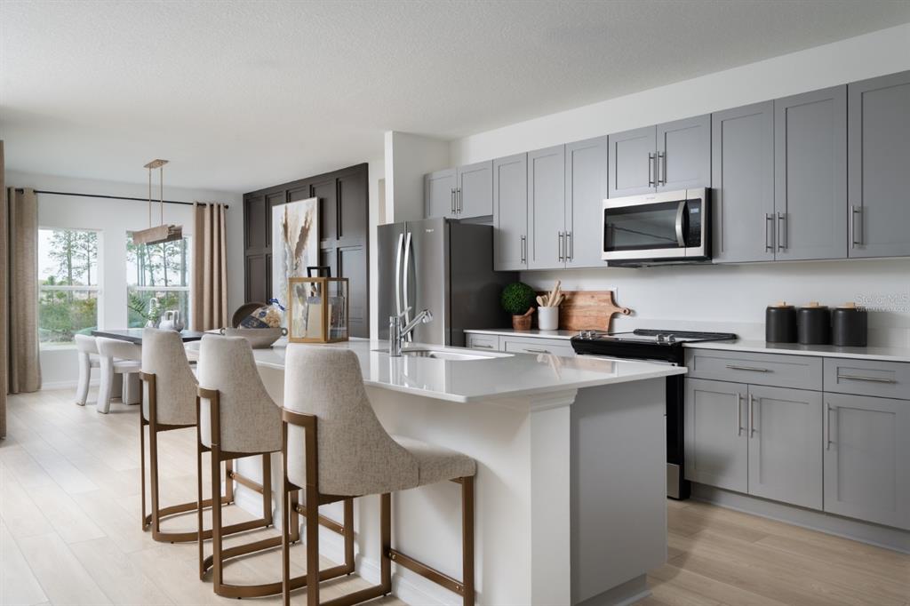 A modern kitchen features gray cabinets, a white quartz island, and three upholstered bar stools — 2338 STILLVIEW PASS, ZEPHYRHILLS, FL