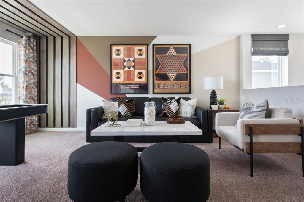 A living room features a black sofa, two black ottomans, and geometric wall art — 2338 STILLVIEW PASS, ZEPHYRHILLS, FL