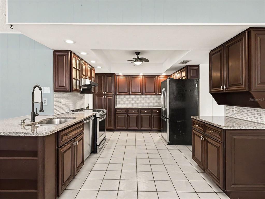 A kitchen features dark wood cabinets, granite countertops, stainless steel appliances, and white tile flooring — 3907 23RD AVENUE W, BRADENTON, FL
