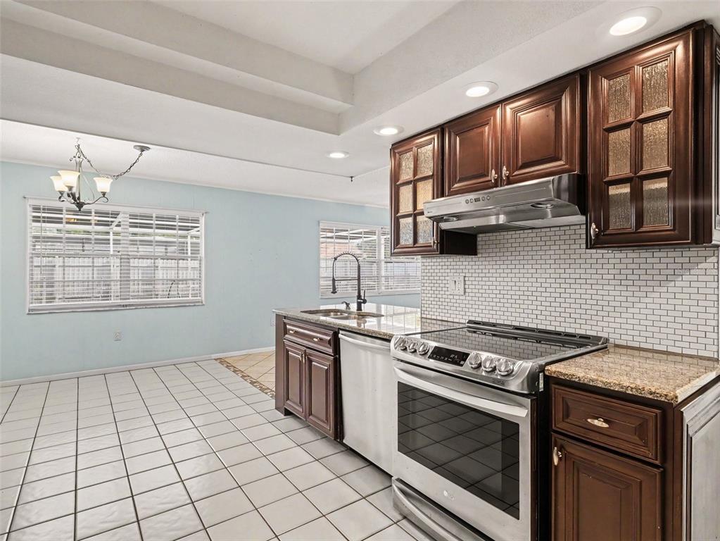 A kitchen with dark wood cabinets, granite countertops, stainless steel appliances, and white tile flooring — 3907 23RD AVENUE W, BRADENTON, FL