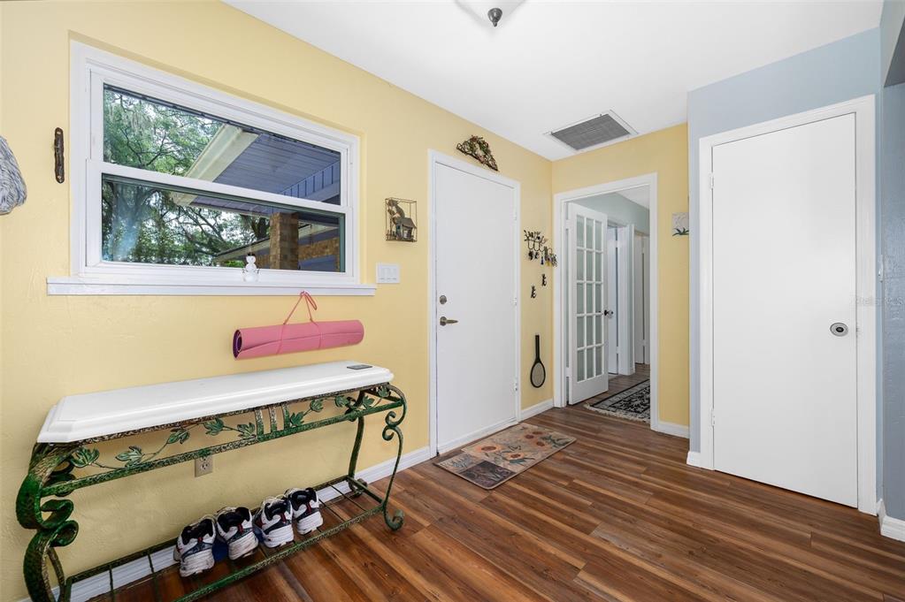 An entryway with yellow walls, wood-look flooring, a white console table, and two white doors — 16422 NE 10TH STREET, GAINESVILLE, FL